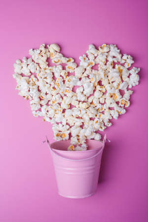 Small pink bucket with popcorn spilled outon background, vertical shotの写真素材