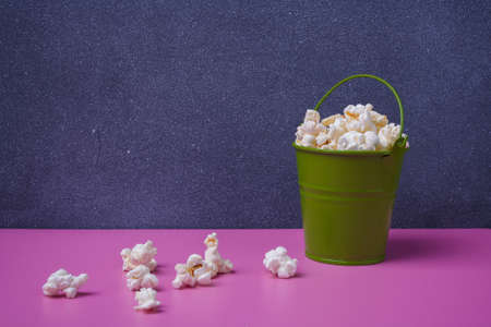 Small green bucket of pop corn on gray and pink background. Some popcorns lying near. Copy space.の写真素材