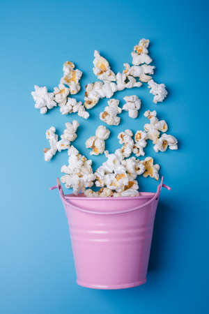 Small pink bucket on blue background with popcorn spilled out, vertical shotの写真素材