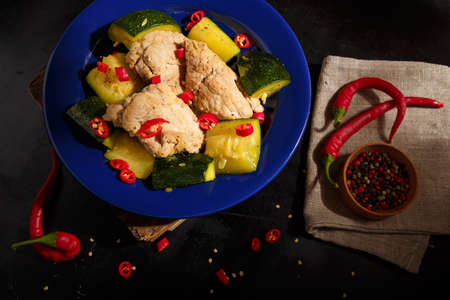 Stew or braised pork with zucchini and hot red pepper served on blue plate, wooden kitchen table background. Meat dish for meal.の写真素材