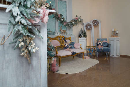 Izmail, Ukraine. December 2020. Merry Christmas decorated room. Festive interior with fir tree, pink sofa, wooden toys, icy roses. Wrapped presentsのeditorial素材