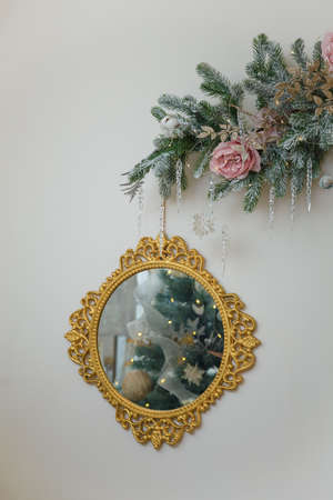 Round golden mirror with decorated Christmas tree reflection. Snowy fir branches with icycles, icy roses hanging on wall. Copy spaceの写真素材