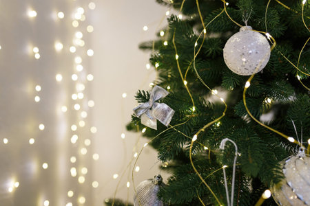 Silver bauble and bow on fir tree branch with garland lights bokeh on background. Beautiful...