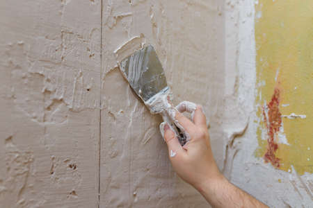 Male hands with spatula using putty for wall, builder making overhaul.の写真素材