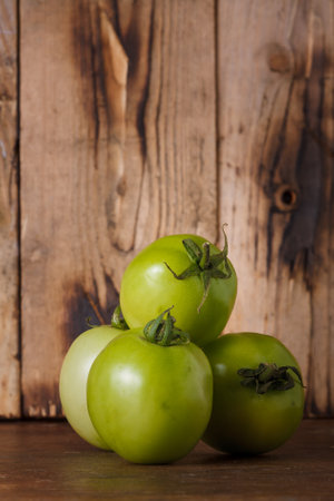 Green tomatoes on brown wooden kitchen rustic background. Farmer fresh organic product. Vegan eco-friendly no animal food. Copy space, vertical shotの写真素材