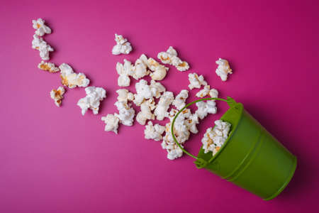 Small green bucket on pink background with popcorn spilled out diagonally, top view, copy spaceの写真素材