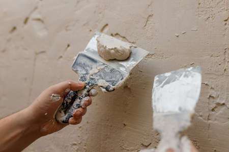 Male hands with spatula using putty for wall, builder making overhaul.の写真素材
