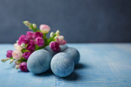 Painted Easter eggs on blue background with purple flowers. Spring holiday, symbolic food. Close up...