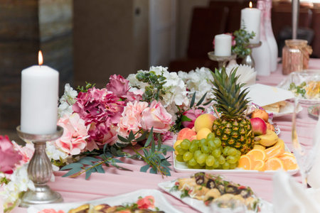 Beautiful festive table with white burning candles and pink flowers, exotic fruit cut. Valentines day romantic dinner or just married wedding presidium.の写真素材