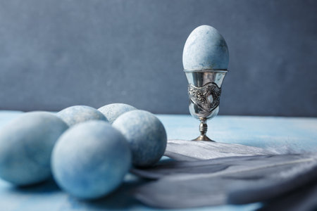 Beautiful painted easter eggs and silver feathers on blue background. One Easter egg in egg cup....