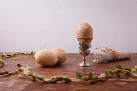 Brown painted Easter egg in silver egg cup on rustic table, white background. Happy Easter, spring...