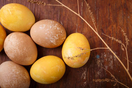 Beautiful Easter eggs colored with natural DIY turmeric and tea paint. Eggs on rustic table with dry branch, top view, close up shotの写真素材