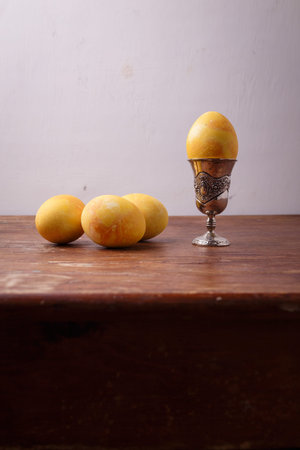 Yellow turmeric painted Easter egg in silver egg cup on rustic table, white background. Happy...
