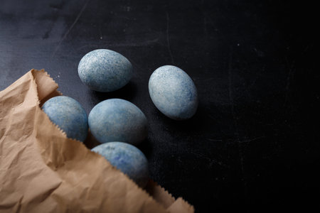 Easter eggs painted blue in craft paper bag on black wooden background. Top view, copy spaceの写真素材