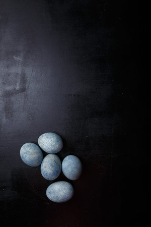 Easter eggs painted blue on black wooden background. Top view, copy space, vertical shotの写真素材