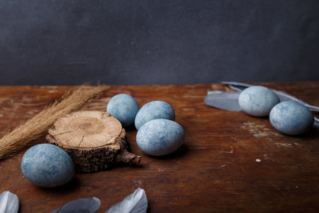 Blue painted easter eggs on brown wooden table with decorative silver feathers. Copy spaceの写真素材