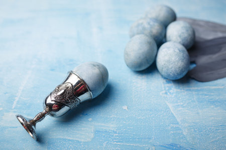 Beautiful painted easter eggs and silver feathers on blue background. One Easter egg in egg cup....