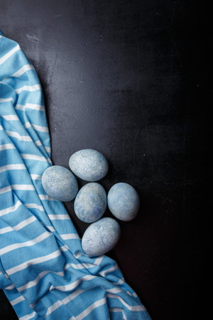 Easter eggs DIY painted blue on black wooden background with striped fabric. Top view, copy space, vertical shotの写真素材
