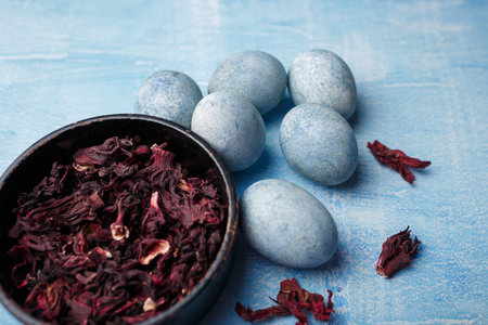 Beautiful DIY painted Easter eggs, dry Hibiscus tea in black bowl. Festive Easter blue wooden...