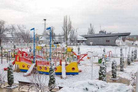 Izmail, Ukraine. February 2022. Navy war ship monument and bright playground in the shape of a ship covered with snow. Empty winter city street with tied thuja bushesのeditorial素材