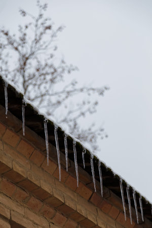 transparent icicles hanging from roof at cold winter day, weather concept, vertical shot