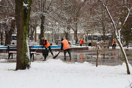 Izmail, Ukraine. February 2022. Janitors or sweepers cleaning city streets from snow with showels and brooms. Snow removal in winterのeditorial素材