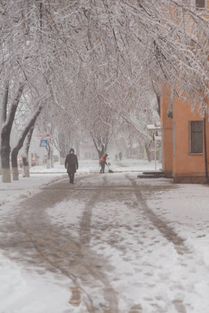 Izmail, Ukraine. February 2022. Janitor in orange jacket cleaning city streets from snow with showel. snow removal in park. Man in covid maskのeditorial素材