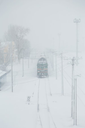 Train on railway station covered with snow. Blizzard, snowstorm and transportation concept. Vertical shotのeditorial素材