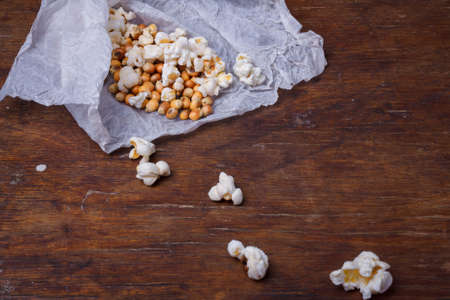 Heap of popcorn on white paper. Some popcorns on wooden rustic background. Vertical shot, top viewの写真素材