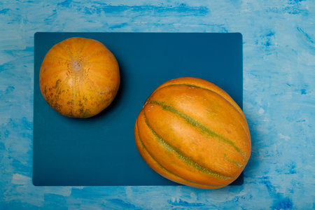 Two sweet ripe yellow melons on blue painted background. Organic seasonal farm fruits concept. Healthy vegan food. Copy space.の写真素材