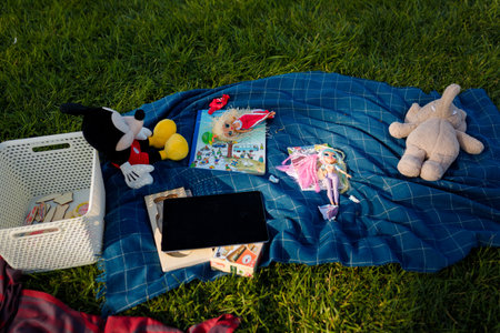 Izmail, Ukraine. May 2021. Children toys, Mickey Mouse, book, tablet on blue plaid on green grass...