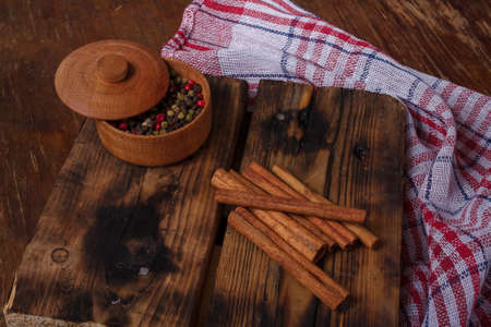 Pot of aromatic pepper set, allspice peas, cinnamon sticks on wooden kitchen board on country table. Flavourings, seasoningsの写真素材