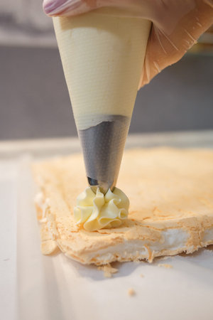 whipped cream squeezing from pastry cone-shaped bag on meringue sheet. Baking and making of meringue...