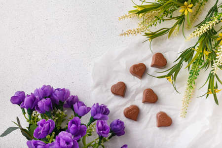 Izmail, Ukraine. 14 February 2022. Heart shaped chocolates Milka, violet and yellow flowers on white paper. Valentines day sweetsのeditorial素材