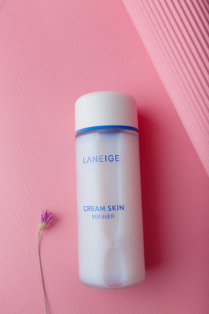 zmail, Ukraine. March 2022. Laneige cream skin refiner bottle on pink background with flower. Korean face skin care cosmeticsのeditorial素材