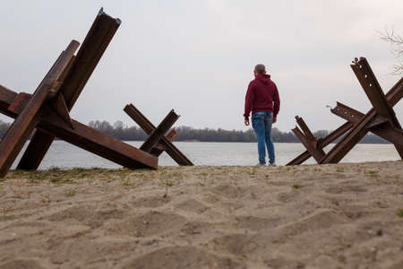 Ukrainian man among anti-tank czech hedgehogs on river bank. Stop Russian military agression, war invasion and genocide in Ukraine 2022の写真素材