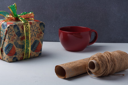 Christmas present, dark red cup and craft paper roll with jute rope spool on white table. Holidays sweets diy packaging, hot winter drinkの写真素材