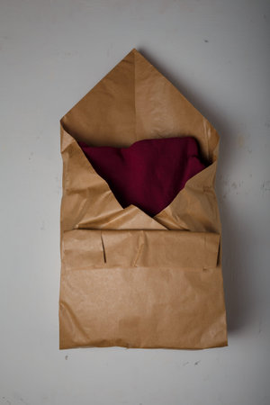 Burgundy cotton hoodie in natural paper package on white background. Eco-friendly product parcel wrapping. Care for environmentの写真素材