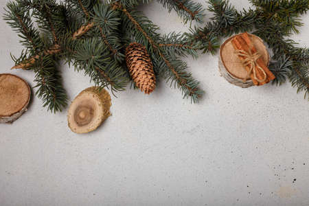 Blue fir tree branch with cone, wooden cut and cinnamon sticks on white wooden background. Christmas card, copy spaceの写真素材