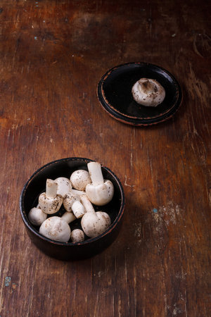 Wooden bowl of fresh raw champignon mushrooms on kitchen table. Autumn harvest, seasonal jrganic vegan food, healhty eating habits.の写真素材