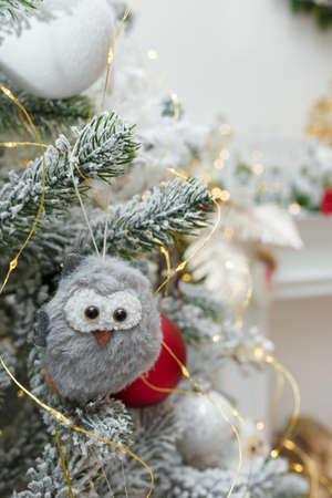 grey fur and fabric owl toy hanging on fir tree branch covered with artificial snow and golden garland lights. Christmas backgroundの写真素材