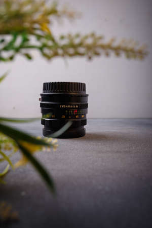 Izmail, Ukraine. April 2022. USSR Helios lens for photo camera on grey background with yellow flowers. Old photo equipment, lens brandのeditorial素材