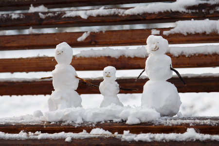 Three small snowmen father mother and child on the bench, beautiful family symbolの写真素材