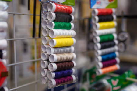 soft focused close up shot of sewing kit, multicolored thread spools in plastic packages in store,...