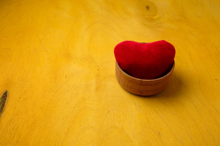 Red heart soft toy in wooden bowl on bright yellow background, copy space. valentines day love symbol, small souvenir, decorの写真素材