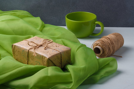Wrapped Christmas present box in craft paper with jute rope, green fabric, cup on white background....