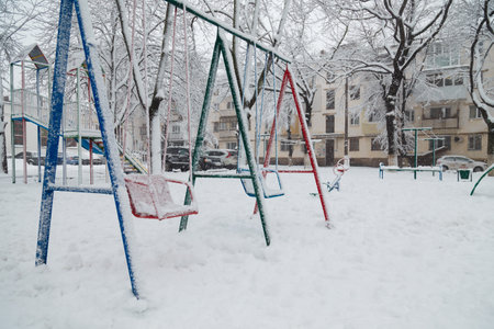 Bright colorful children playground covered with snow on winter snowy background. Snowfall weater, blizzard or snowstormの写真素材