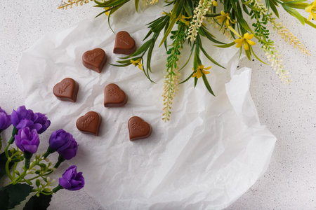 Izmail, Ukraine. 14 February 2022. Heart shaped chocolates Milka, violet and yellow flowers on white...