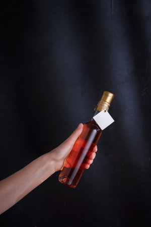 Hand holding bottle of pink wine with template label, no brand. Riesling, chardonnay, sauvignon blanc. Alcohol beverage on black backgroundの写真素材