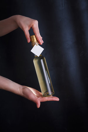 Hands holding bottle of white wine with template label, no brand. Riesling, chardonnay, sauvignon blanc. Alcohol beverage on black backgroundの写真素材